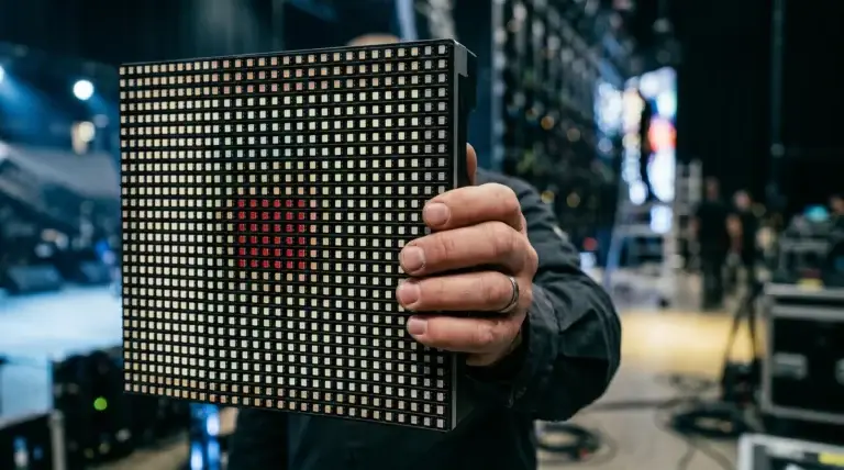Technician holds up a single LED panel module showing the pixel cluster grid and a red test pattern during pre-show LED wall calibration